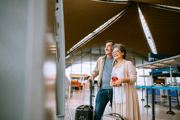 Husband and wife at the airport looking out large glass window happily