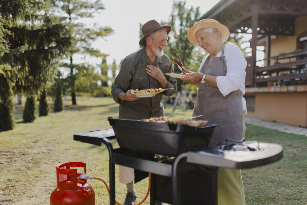 Older couple cooking together on a backyard grill.